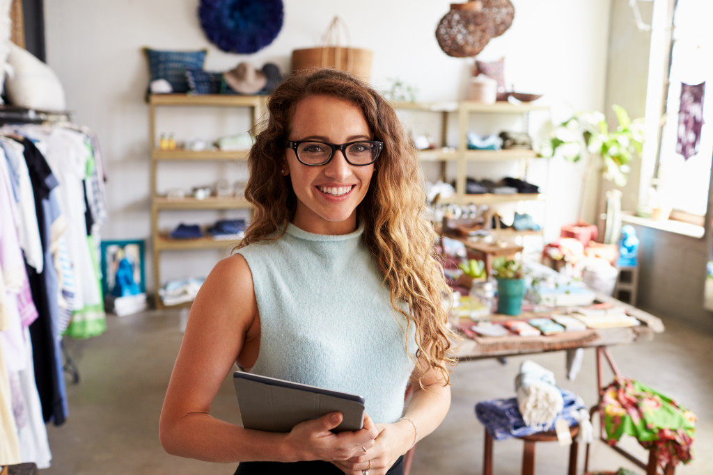 A business owner smiles while holding a tablet inside her brick and mortar shop for clothes and home goods