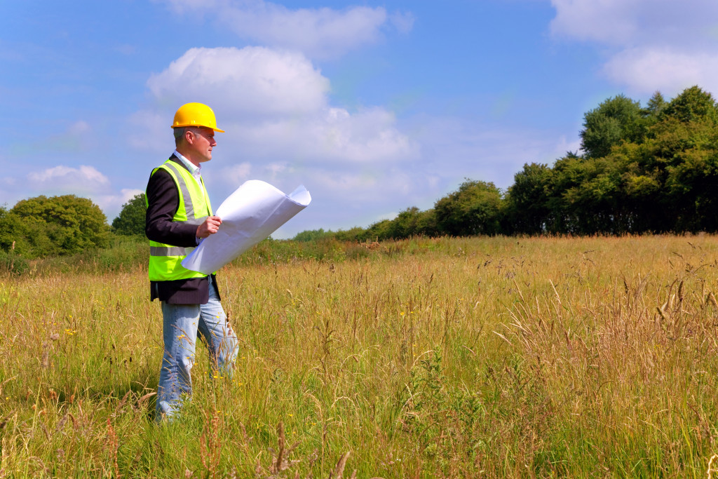 A professional holding a plan while surveying a land