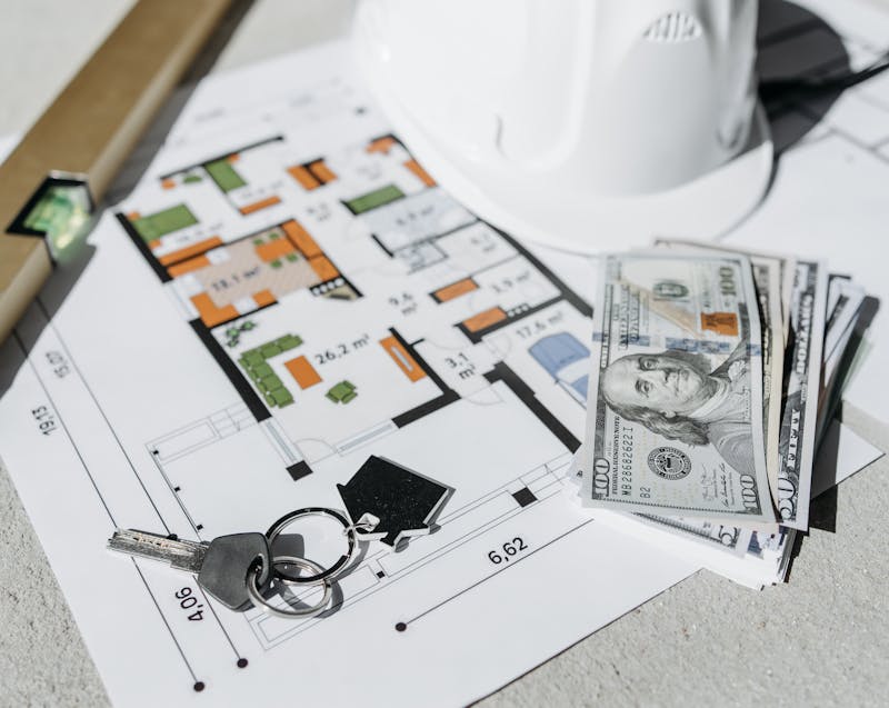 a home construction plan, dollar bills, and house keys
